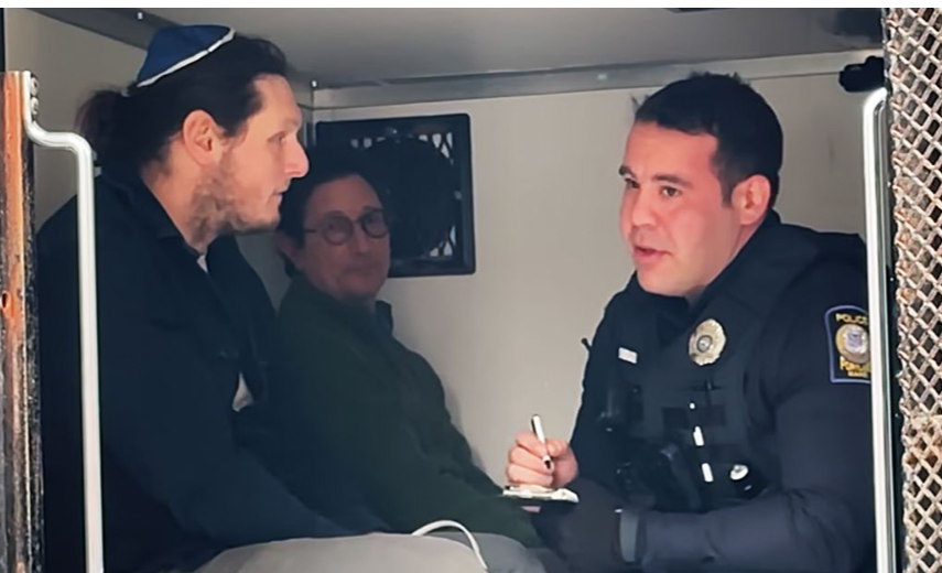 Eric in the back of a police van wearing a yarmulke with an offier and other arestees after a protest
