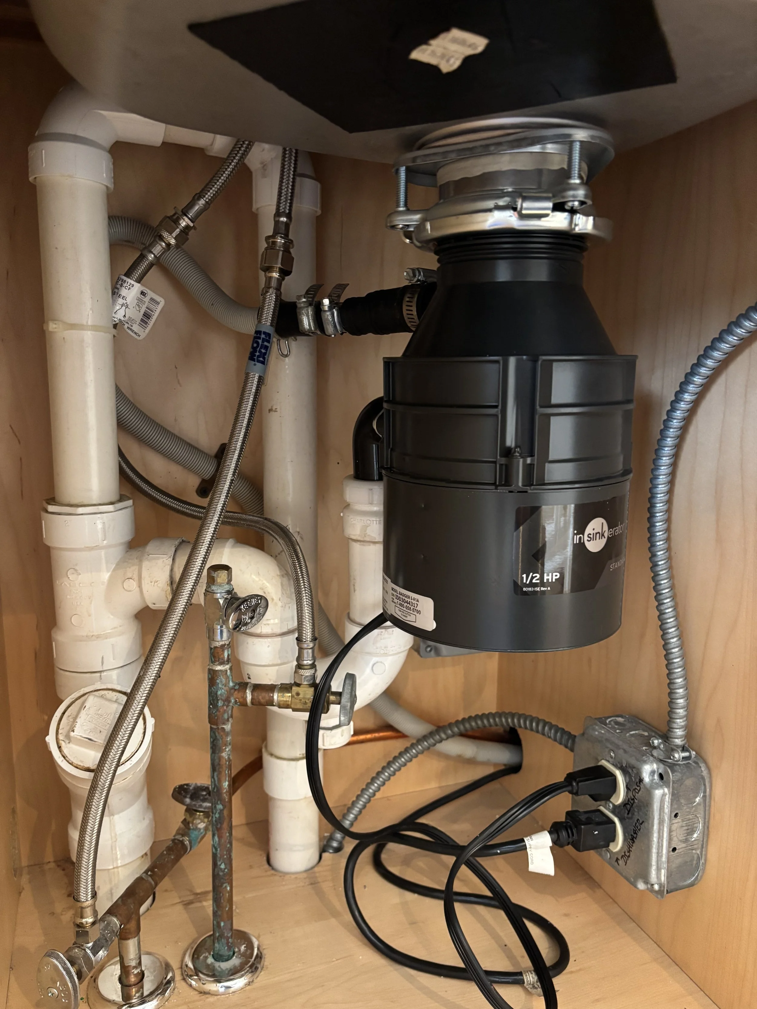 Under-sink plumbing with a garbage disposer unit, pipes, water supply lines, and electrical wiring.