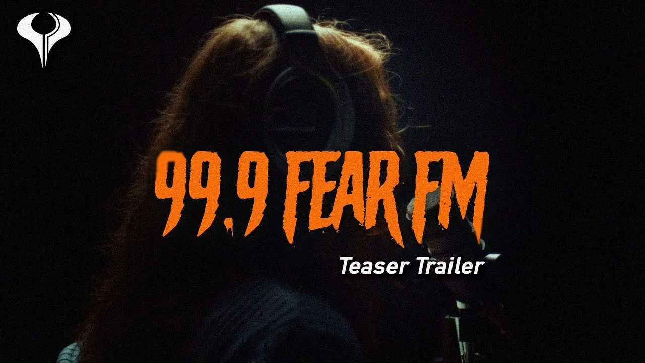 A person with long hair wearing headphones speaking into a microphone in a dark recording studio, with the text "99.9 FEAR FM" and "Teaser Trailer" overlaid.