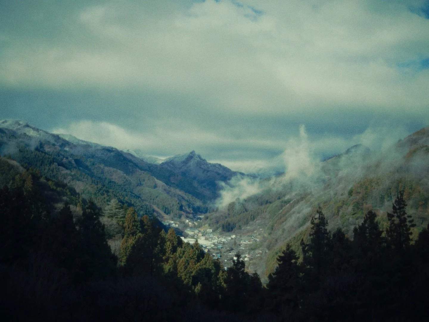 Mountain valley with forested hills, small town, mist, and clouds in the sky