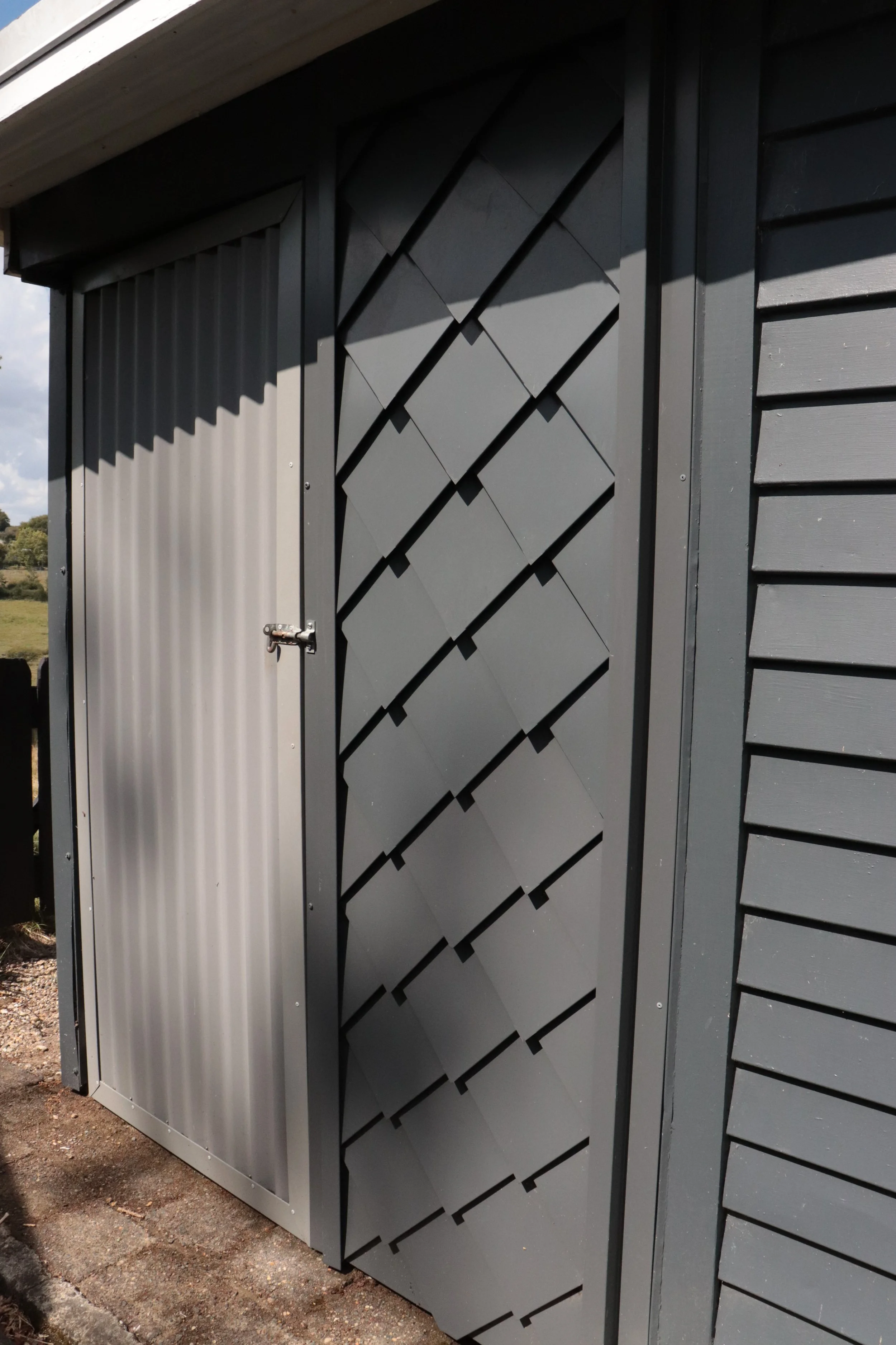 Gray storage shed with a metal door and decorative wall panel.
