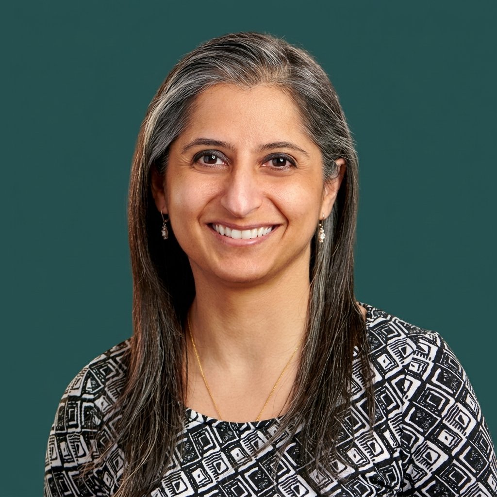 A woman with long gray hair wearing earrings, a necklace, and a patterned black and white top, smiling at the camera against a green background.
