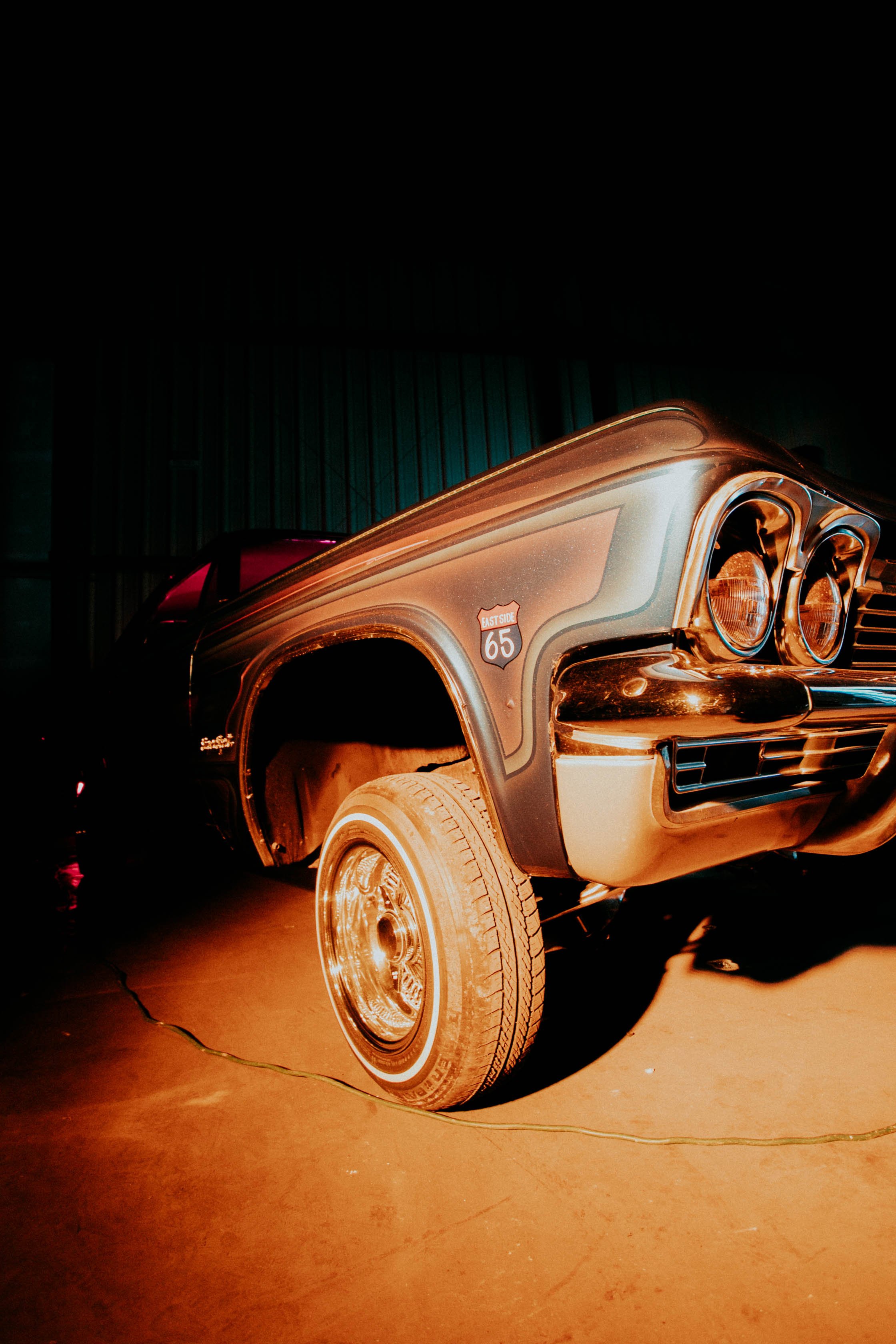 Close-up of a vintage black and gold car with a shiny finish, showing the front right side, headlight, and tire, parked indoors.