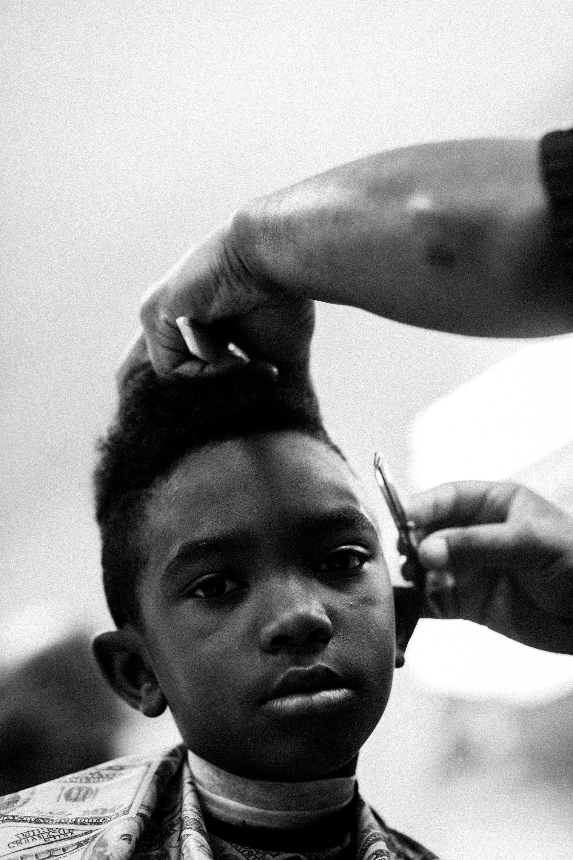 A young boy getting his hair cut by a barber in black and white.