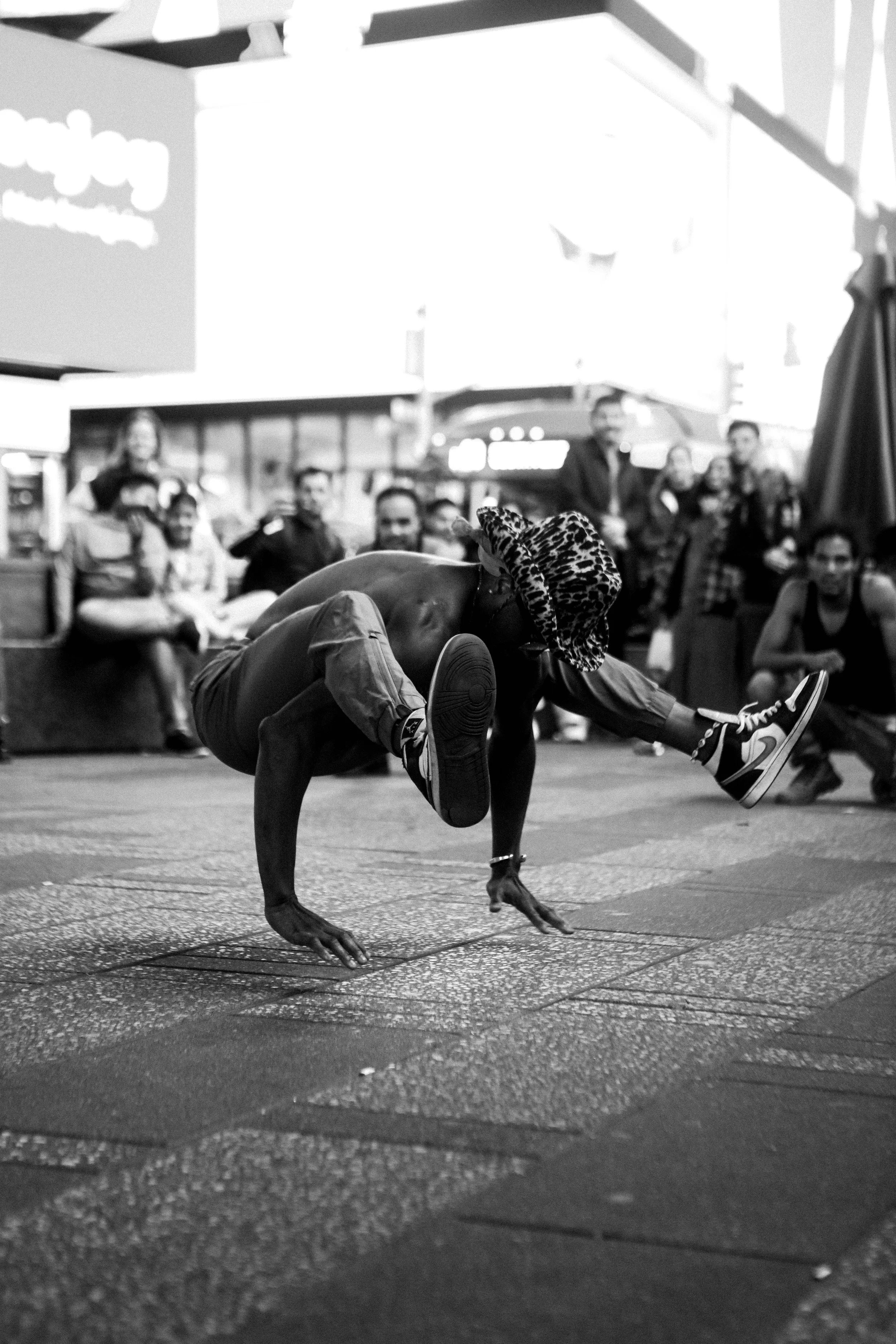 A street performer doing a breakdancing move on the sidewalk with a crowd in the background.