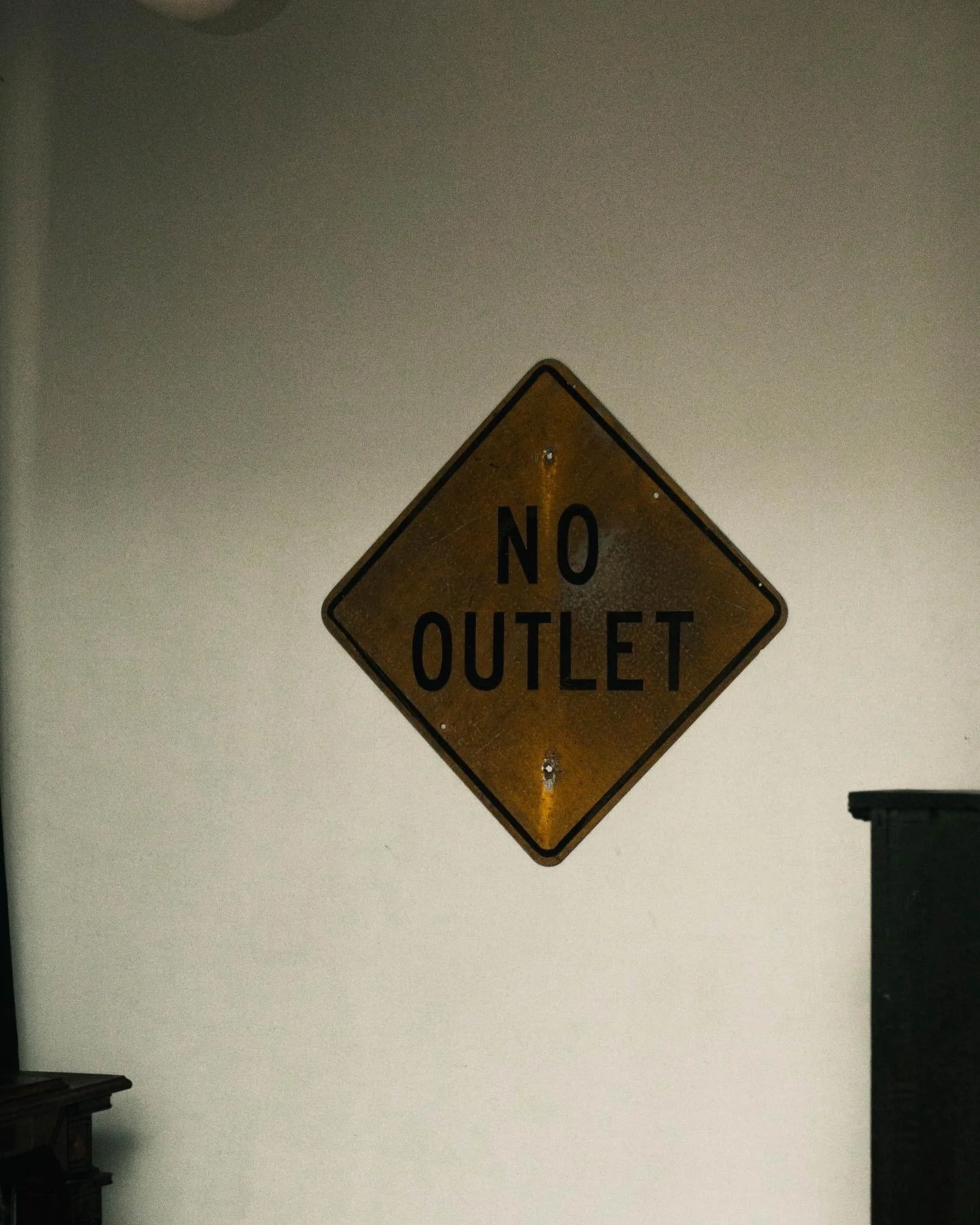 A wall sign that reads 'No Outlet' in black letters on a yellow diamond-shaped background.