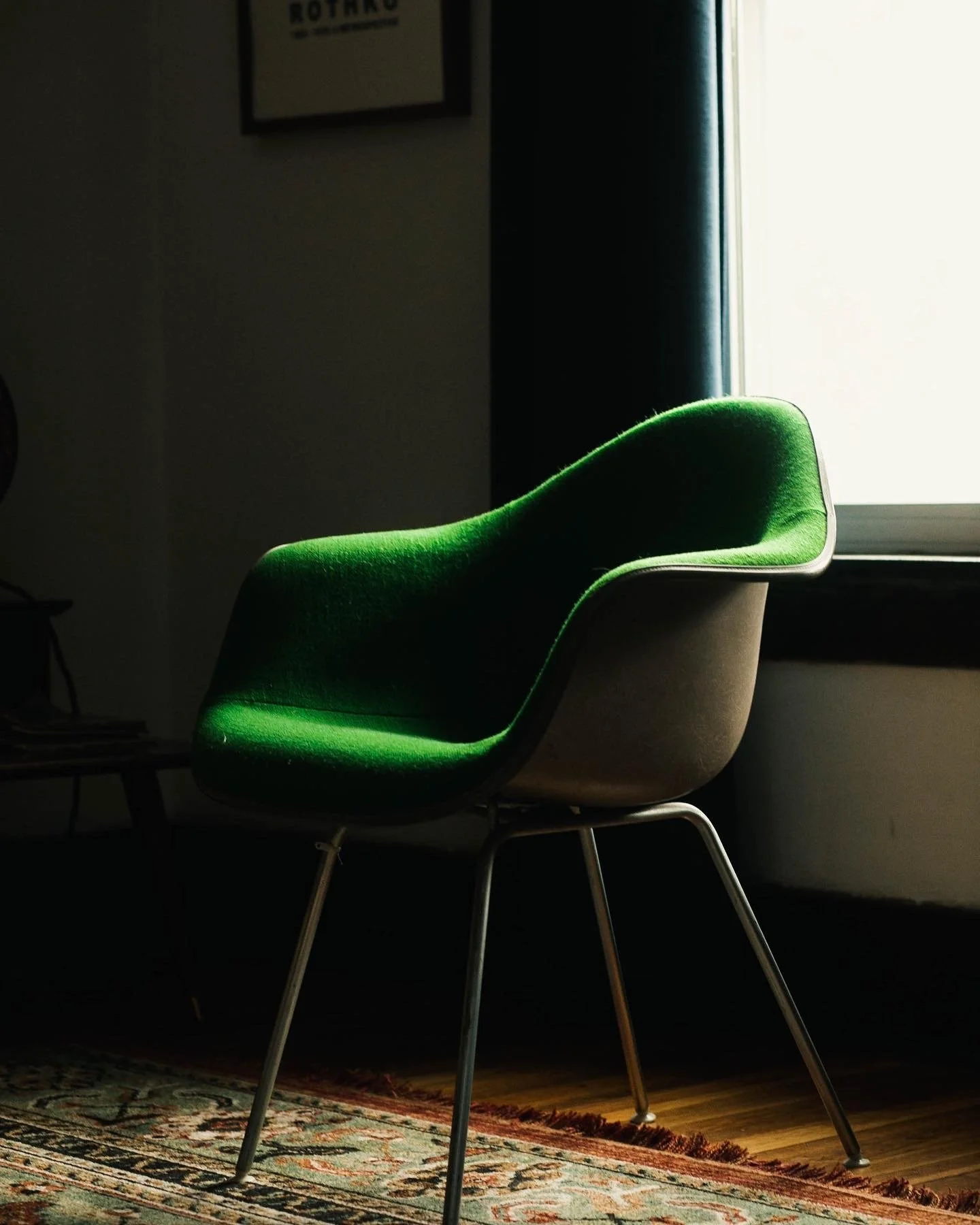 Green upholstered chair with metal legs near a window, casting light on the seat