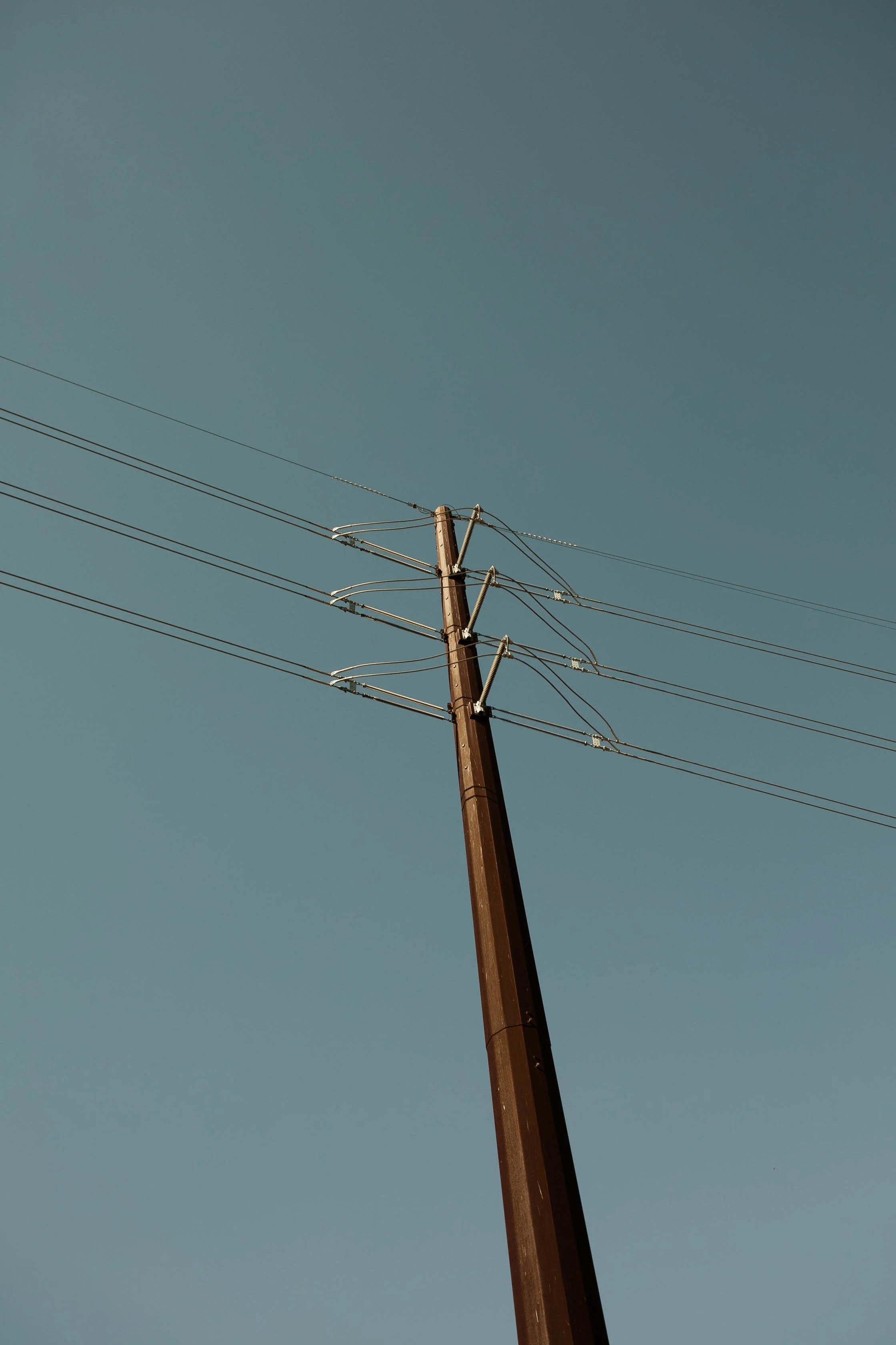 A tall wooden utility pole with electrical wires against a clear blue sky.