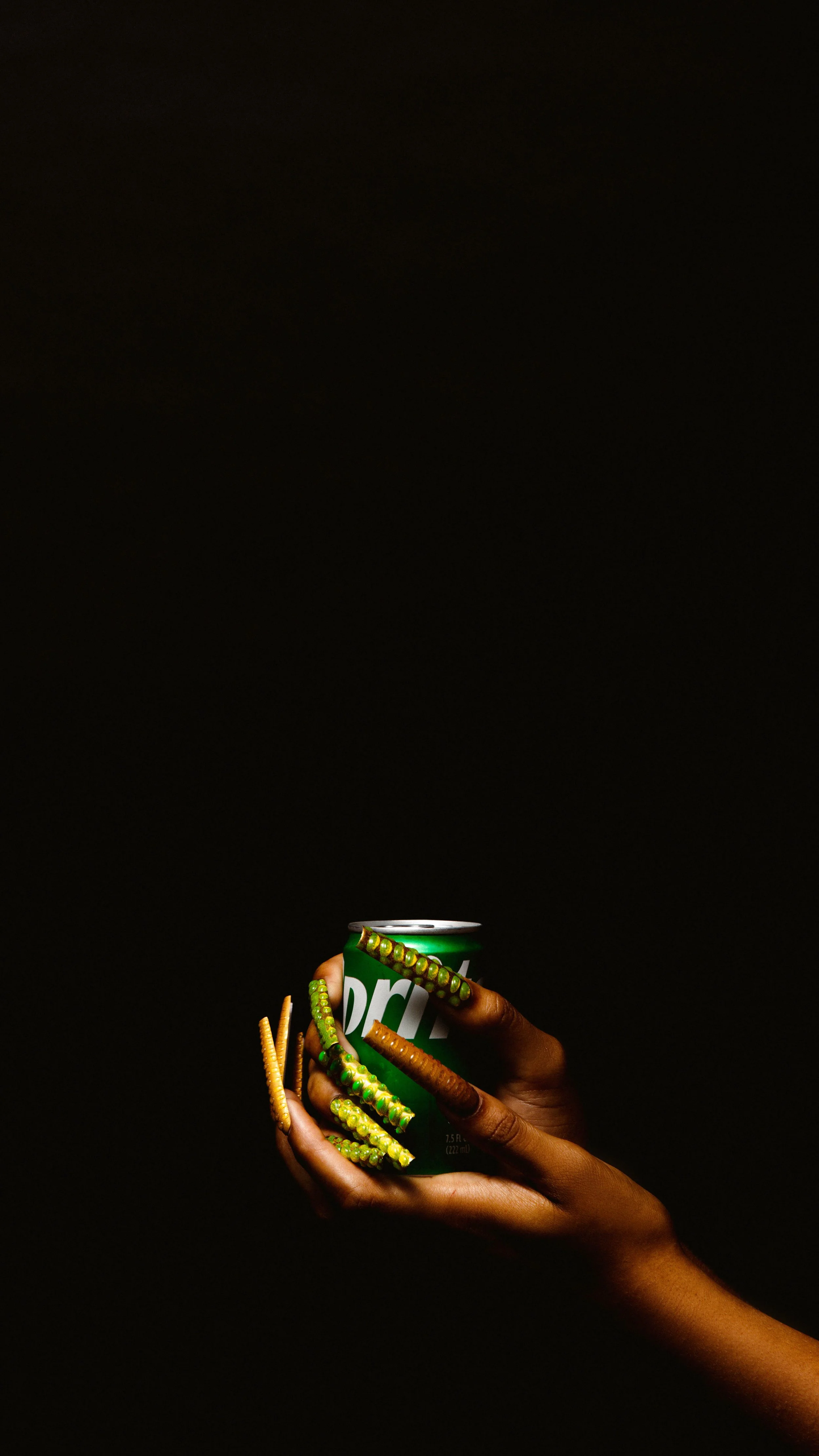 Hand holding a Sprite soda can with decorated fingernails against a dark background.