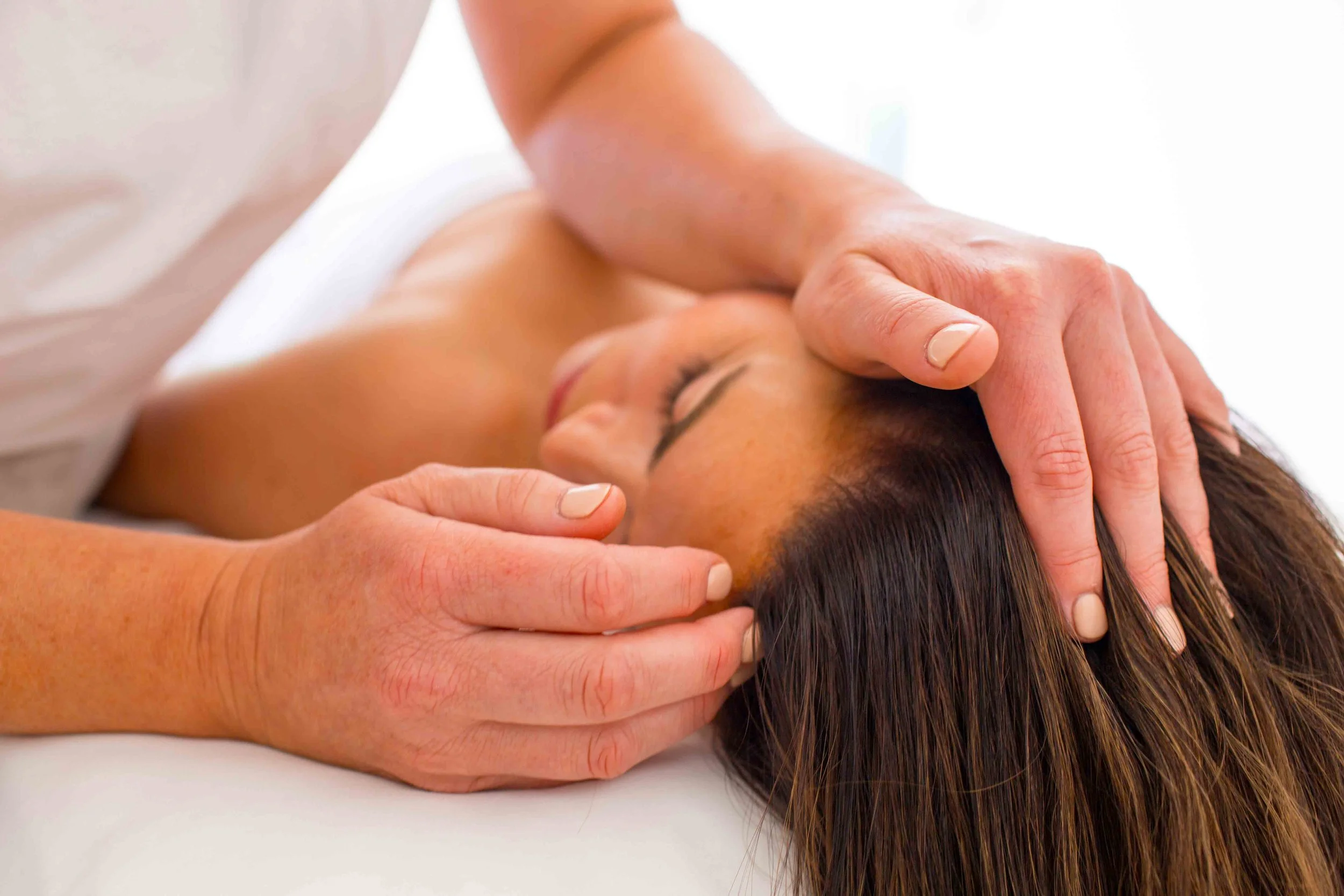 Person receiving a massage with hands on the head and neck, lying face down.