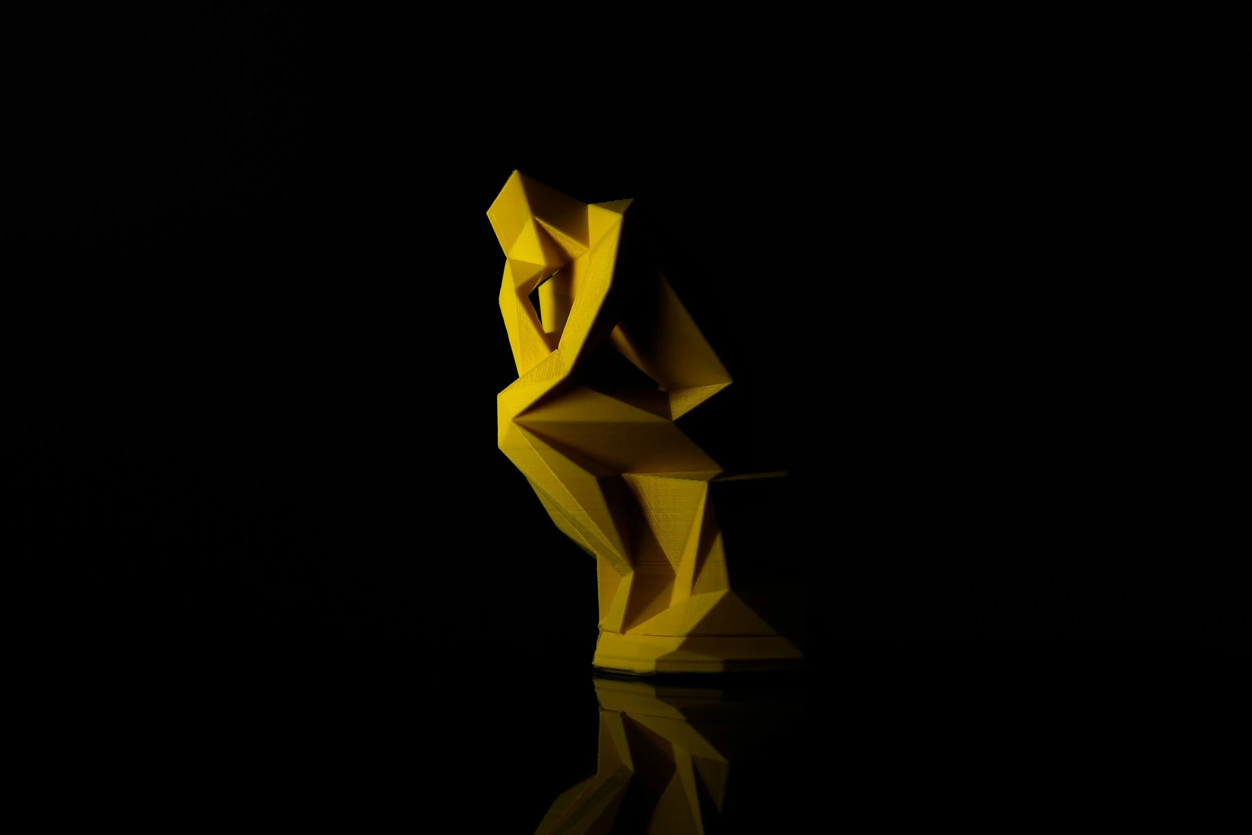Yellow origami lion sculpture reflecting on a black surface against a black background.