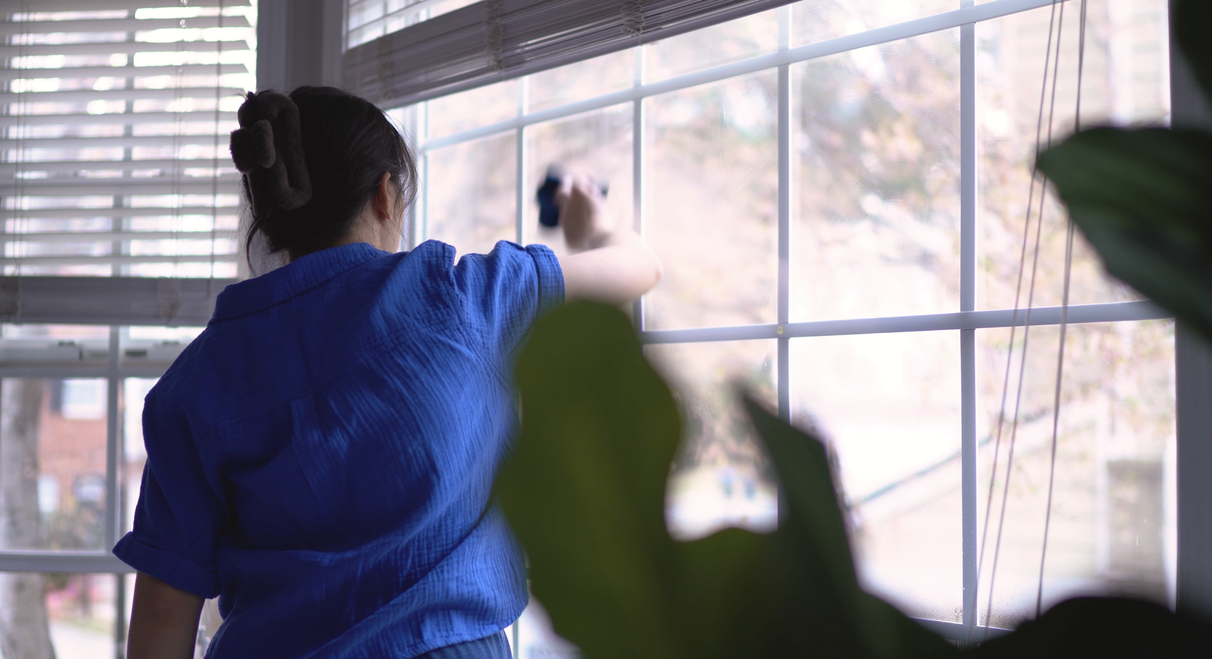 Professional residential home cleaner wiping interior windows in a bright, well-kept home
