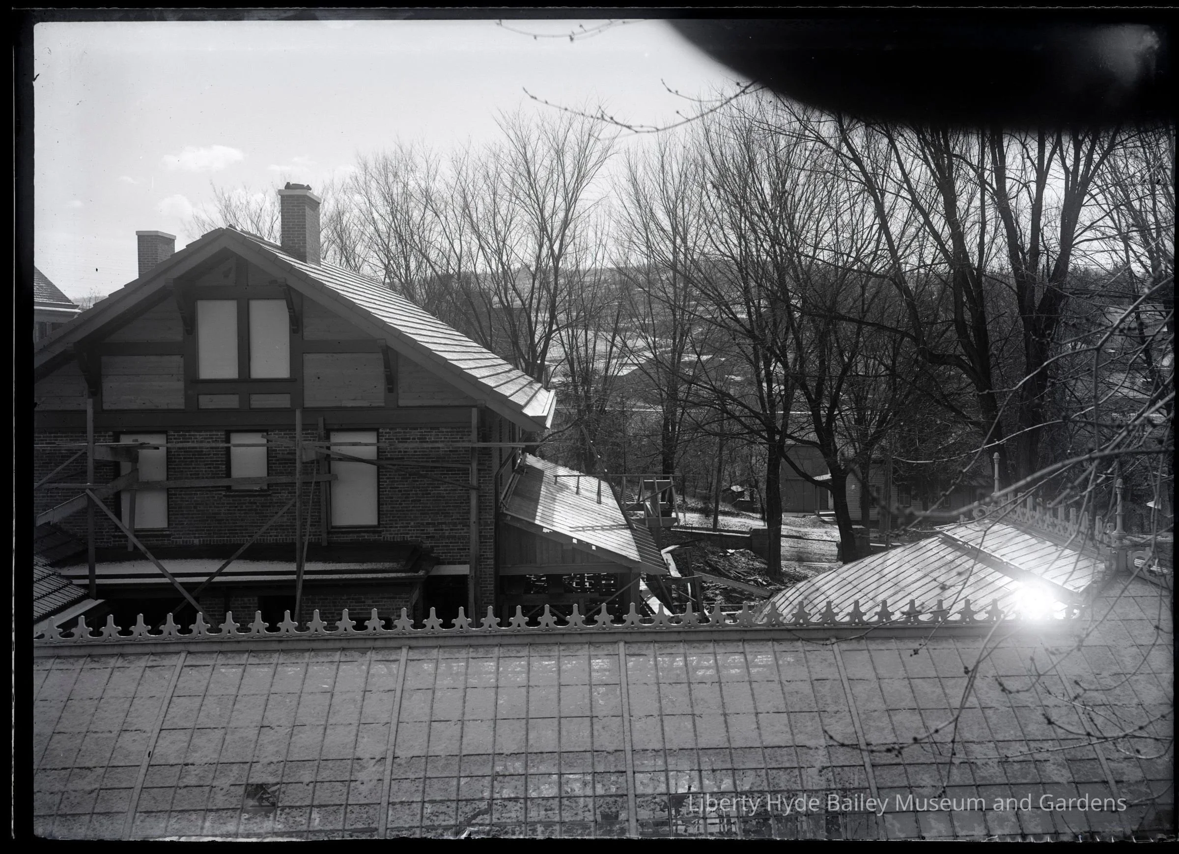 View of the upper part of the Liberty Hyde Bailey house from the upstairs balcony of the old Carriage House, with the roofline of the original Henry Sage conservatory in the foreground. A light snow ices the image. The valley of Ithaca slopes behind.