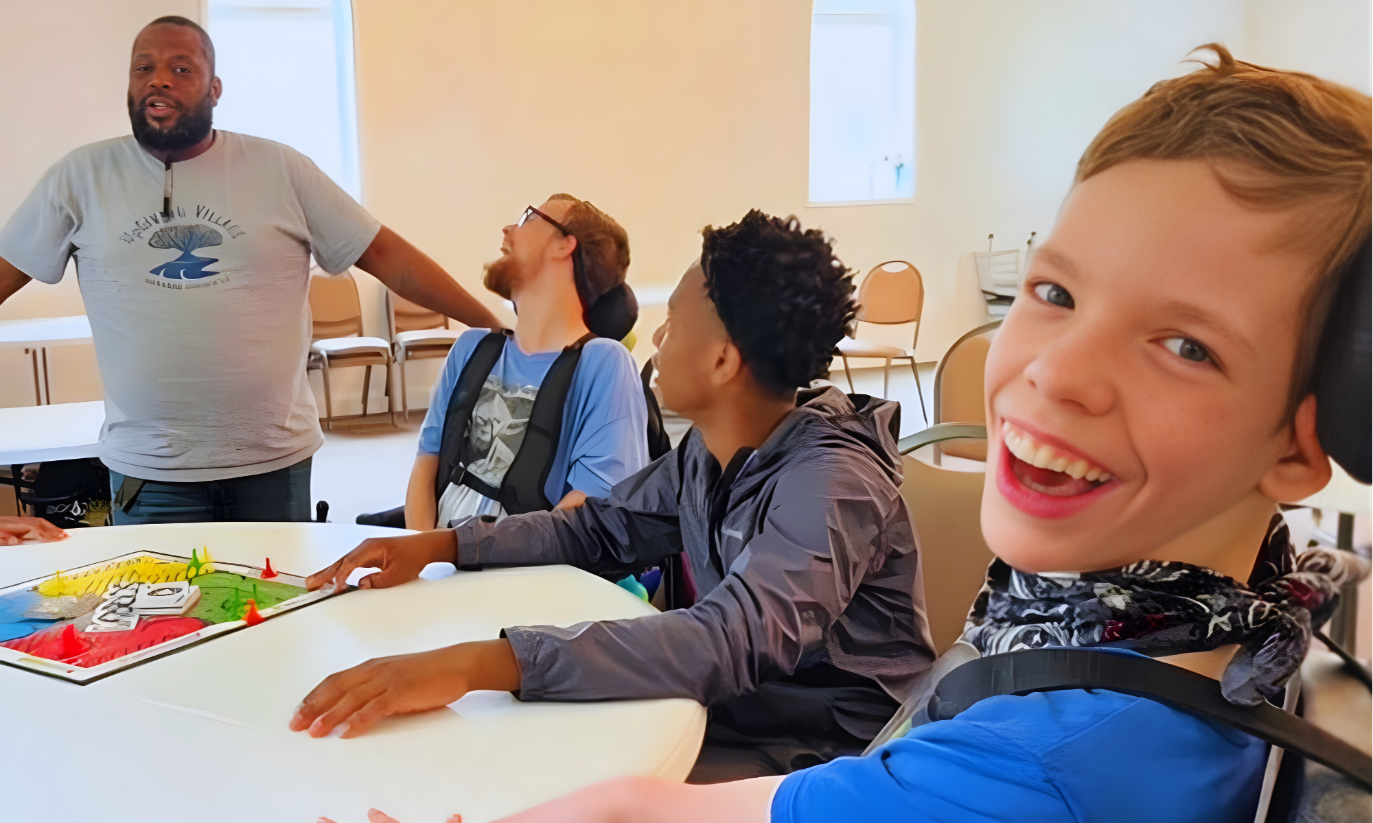 A group of diverse children sitting around a table, smiling and laughing during an activity led by an adult male. The activity is designed to encourage connection, learning, and community engagement.