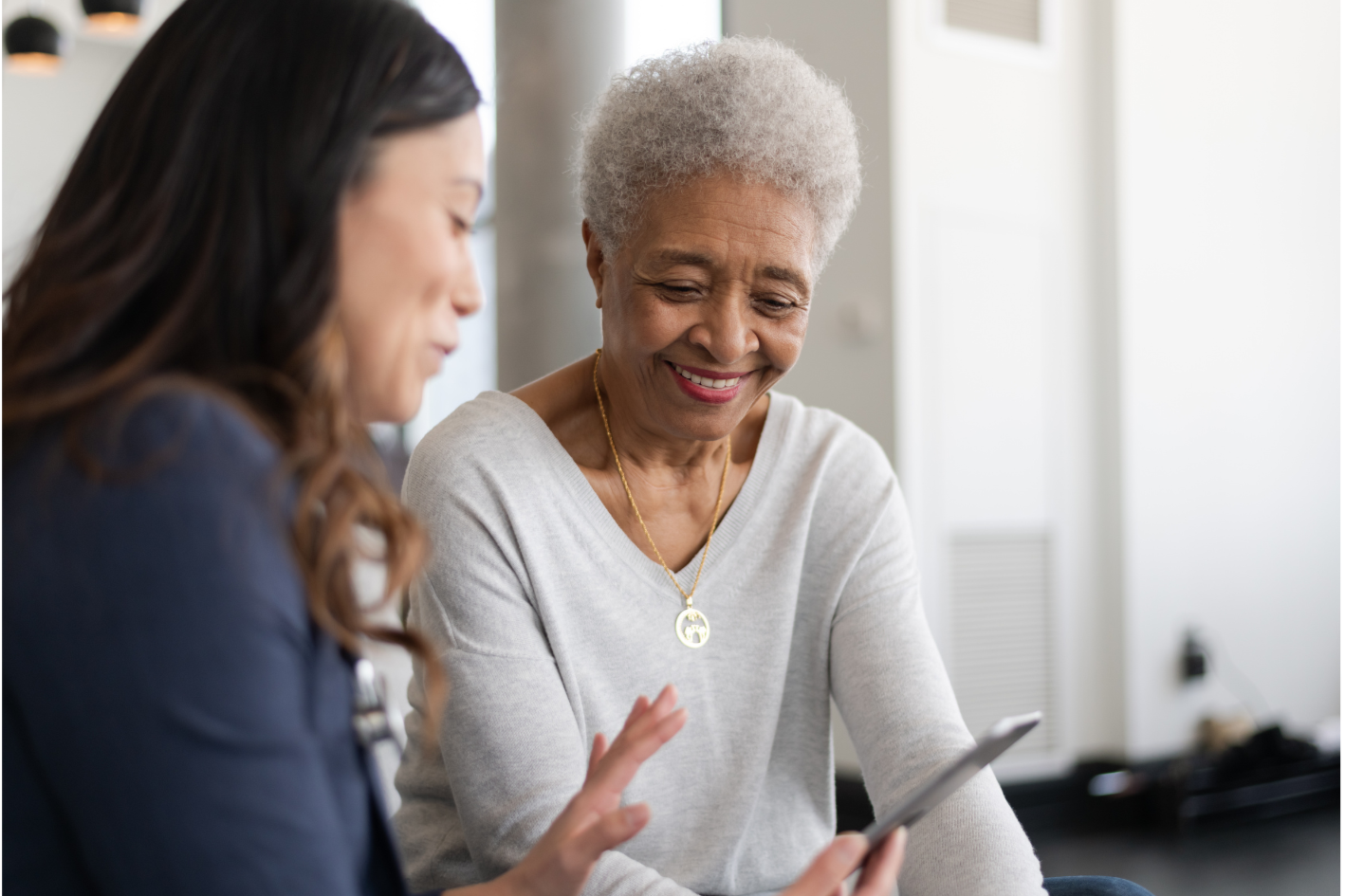 Two women sharing a meaningful moment of connection and conversation in a supportive environment, sitting together, looking at a tablet, and smiling.