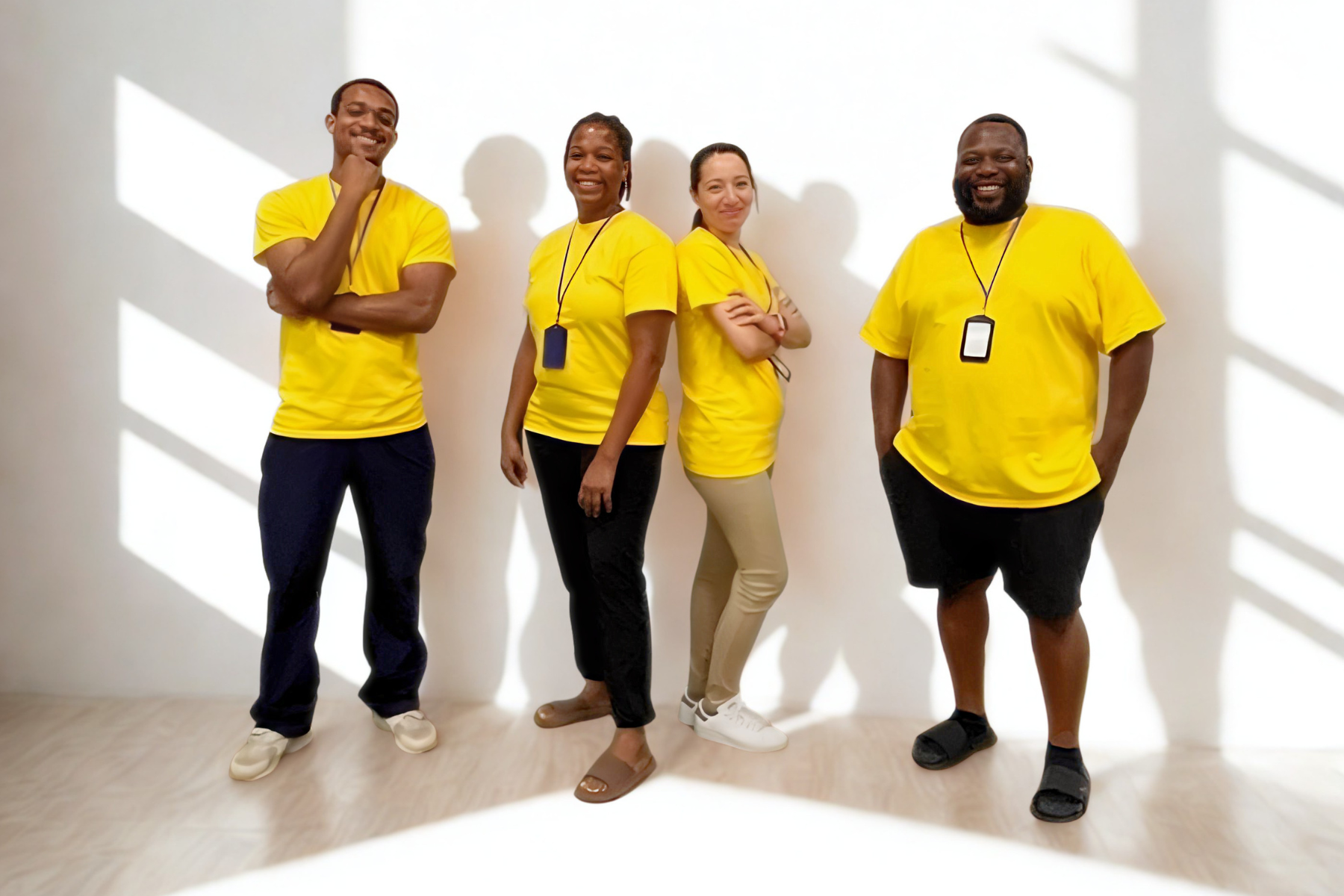 Up Giving Village volunteers standing together in a room, wearing matching yellow shirts and black or beige pants, smiling and posing for the camera.