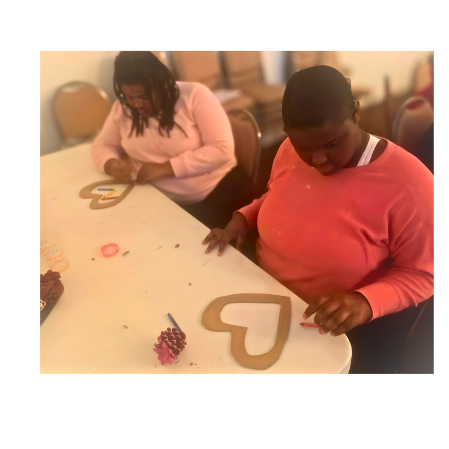 Participants are creating crafts together during a seasonal engagement activity, each working on a heart-shaped craft project with wooden frames, surrounded by festive decorations such as pinecones and holiday ornaments.