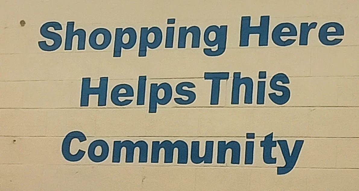 Sign that says "Shopping Here Helps This Community" in blue letters on a white wall.
