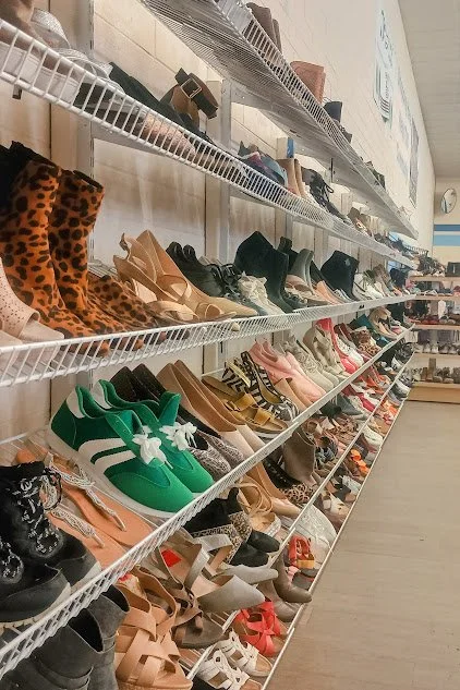 Display of various shoes on white wire shelves in the thrift store aisle.