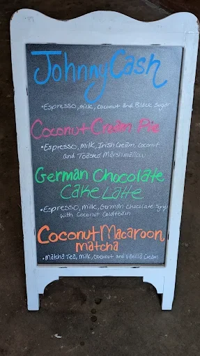 Menu board listing four drinks: Johnny Cash, Coconut Cram Pie, German Chocolate Cake Latte, and Coconut Macaroon Malala, with ingredients mentioned.