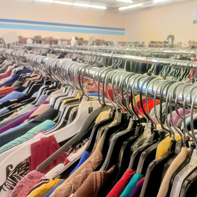 Clothing racks filled with various colorful shirts and garments in the thrift store.