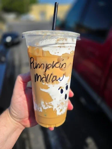 Hand holding a large iced pumpkin mallow latte with a black straw, written on the cup in black marker.