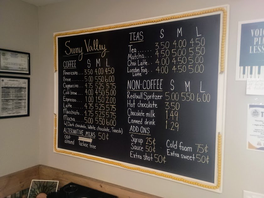 Menu board at Sunny Valley Coffee listing coffee, tea, non-coffee drinks, and add-ons with prices.