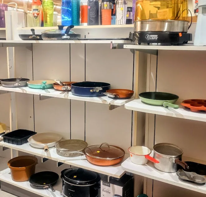 Display of various cookware and pans on white shelves at a store.