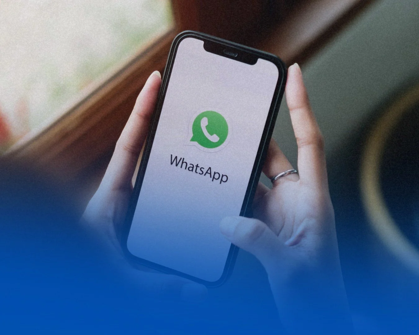 Persona sosteniendo un teléfono móvil con la pantalla que muestra el logo y nombre de WhatsApp.