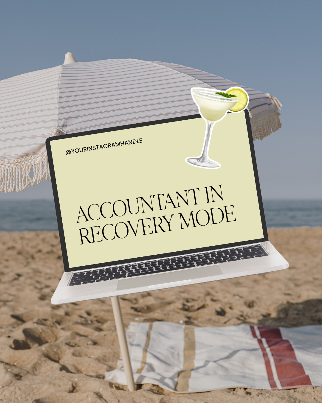 Laptop on the beach with a sign reading 'Accountant in Recovery Mode' and a margarita sticker, under a beach umbrella on sandy ground.