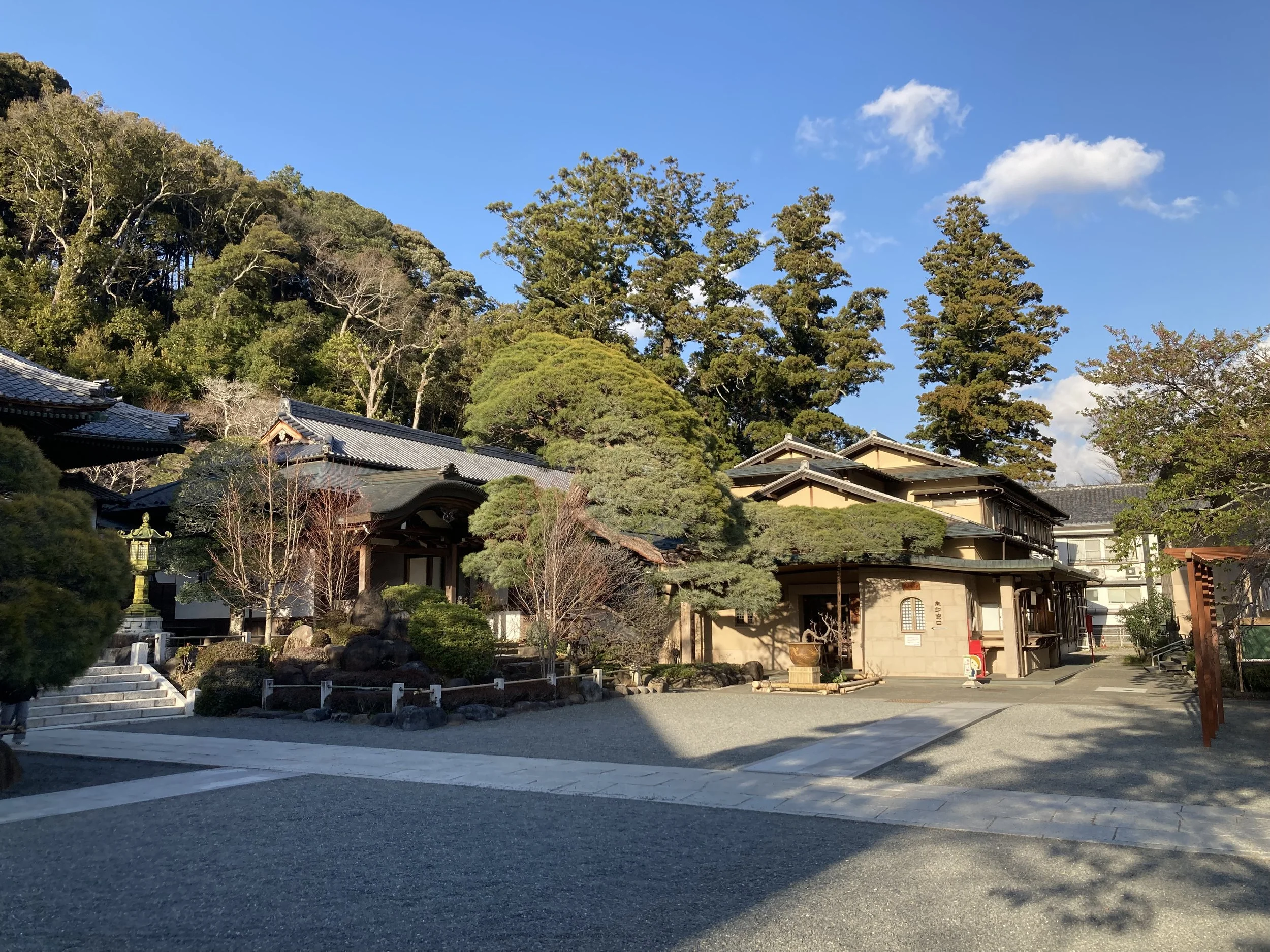 Traditional Japanese building with trees, stone steps, and a blue sky with white clouds.