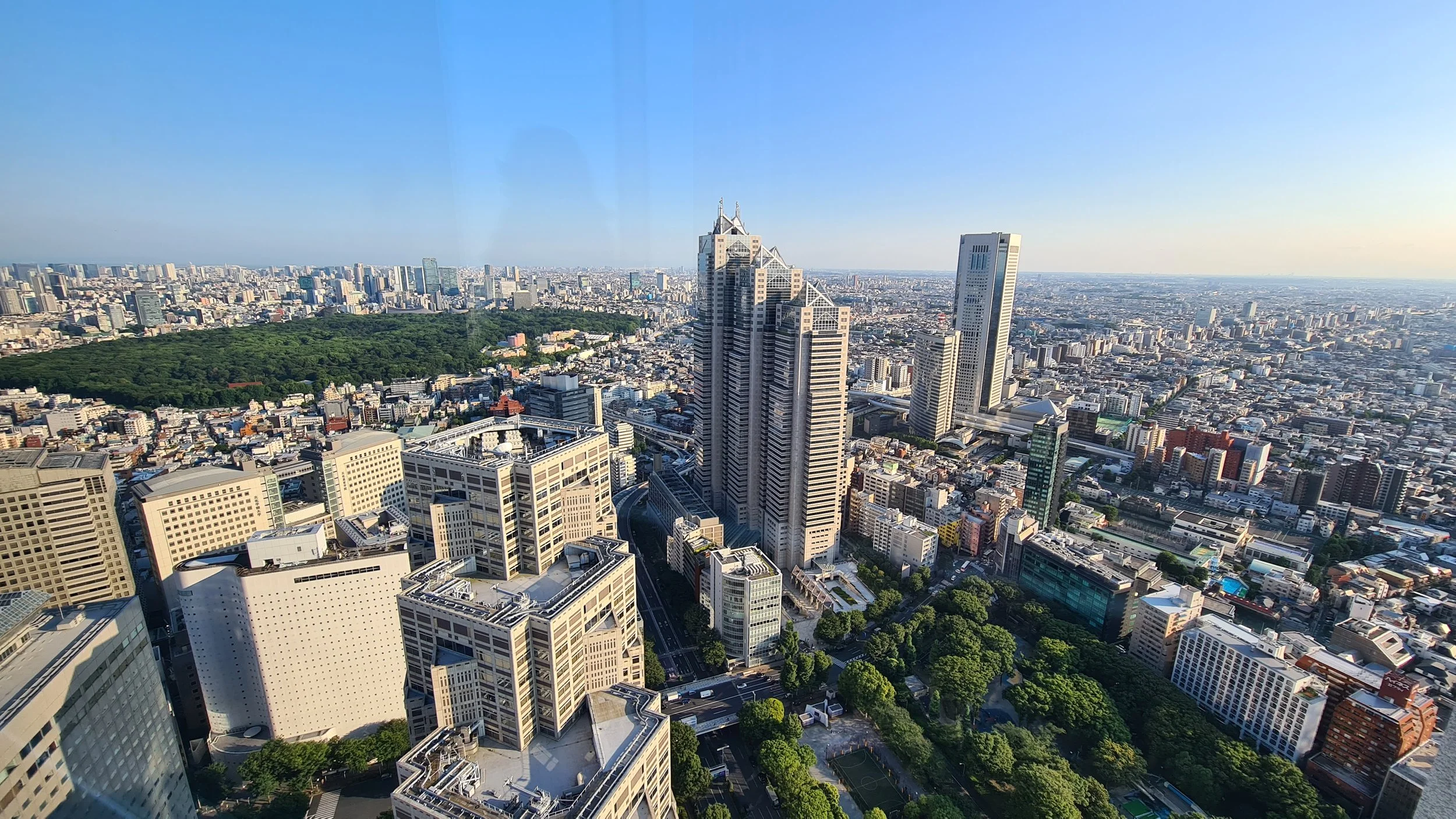 A view of a city skyline with tall skyscrapers, a large green park, and extensive urban landscape under a clear blue sky.