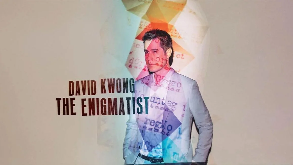 Poster featuring David Kwong in a white suit with a colorful geometric abstract background. The text reads "David Kwong The Enigmatist."