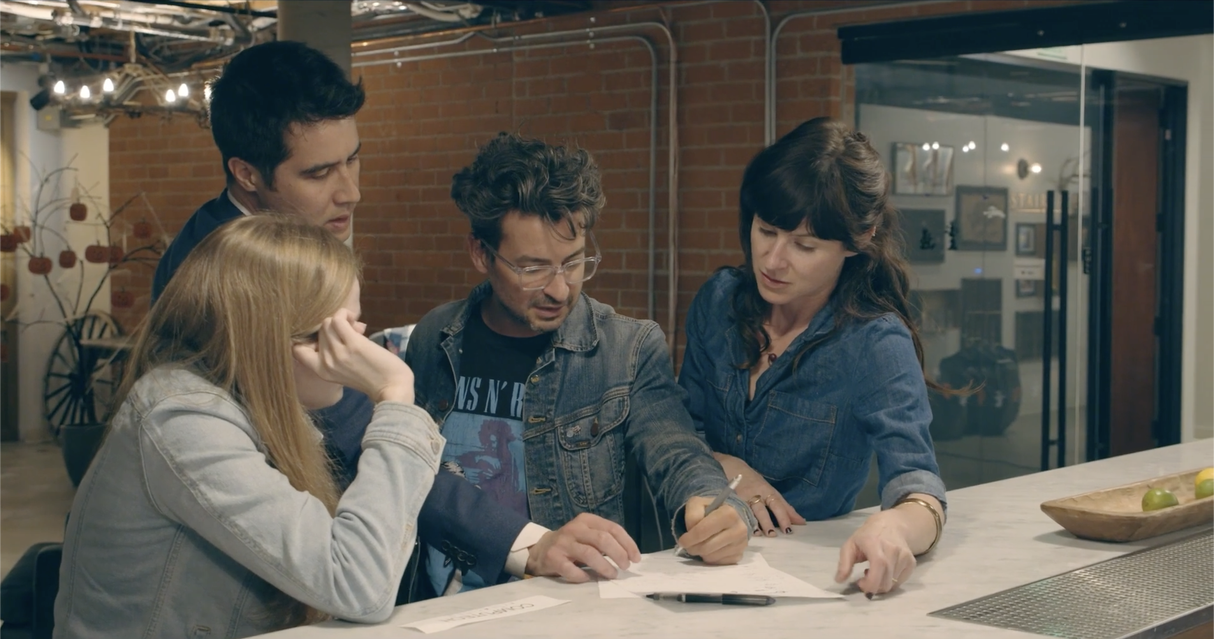David Kwong and three young adults gathered around a white table in a casual indoor setting, working on a puzzle together.