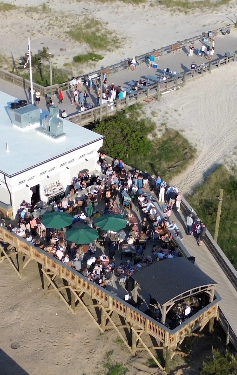 Our crowded outdoor deck, with many people dining under green umbrellas and on tables, adjoining Cupsogue Beach