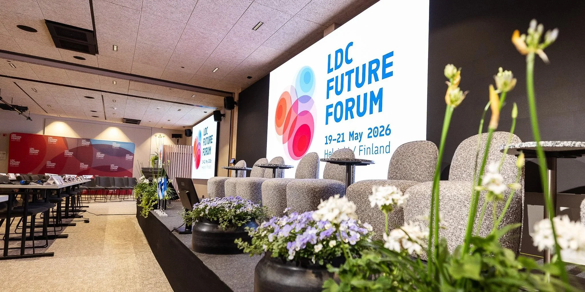 Konferenssali, jossa suuret näytöt, nimitys 'LDC Future Forum', ja pöytiä sekä kukka-asetelmia, järjestetty 19.–21. toukokuuta 2026 Helsingissä, Suomessa.