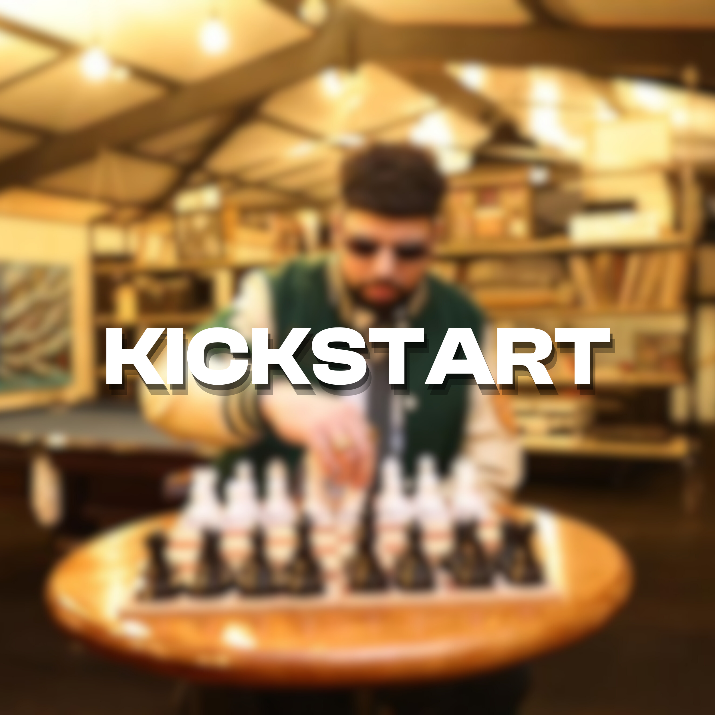 A person wearing sunglasses and a jacket, arranging dominoes on a round wooden table in a cozy, bookshelf-filled room, with the word 'KICKSTART' overlaid.