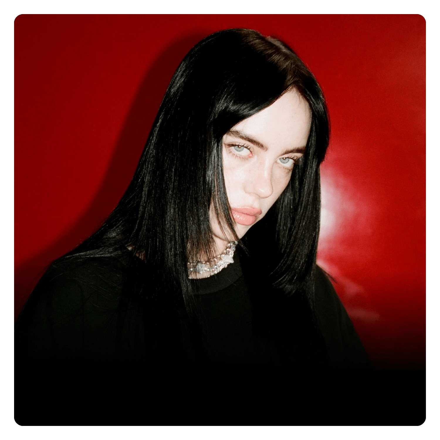 A young woman with long black hair and pale skin, wearing a black top and silver jewelry, posing against a red background.