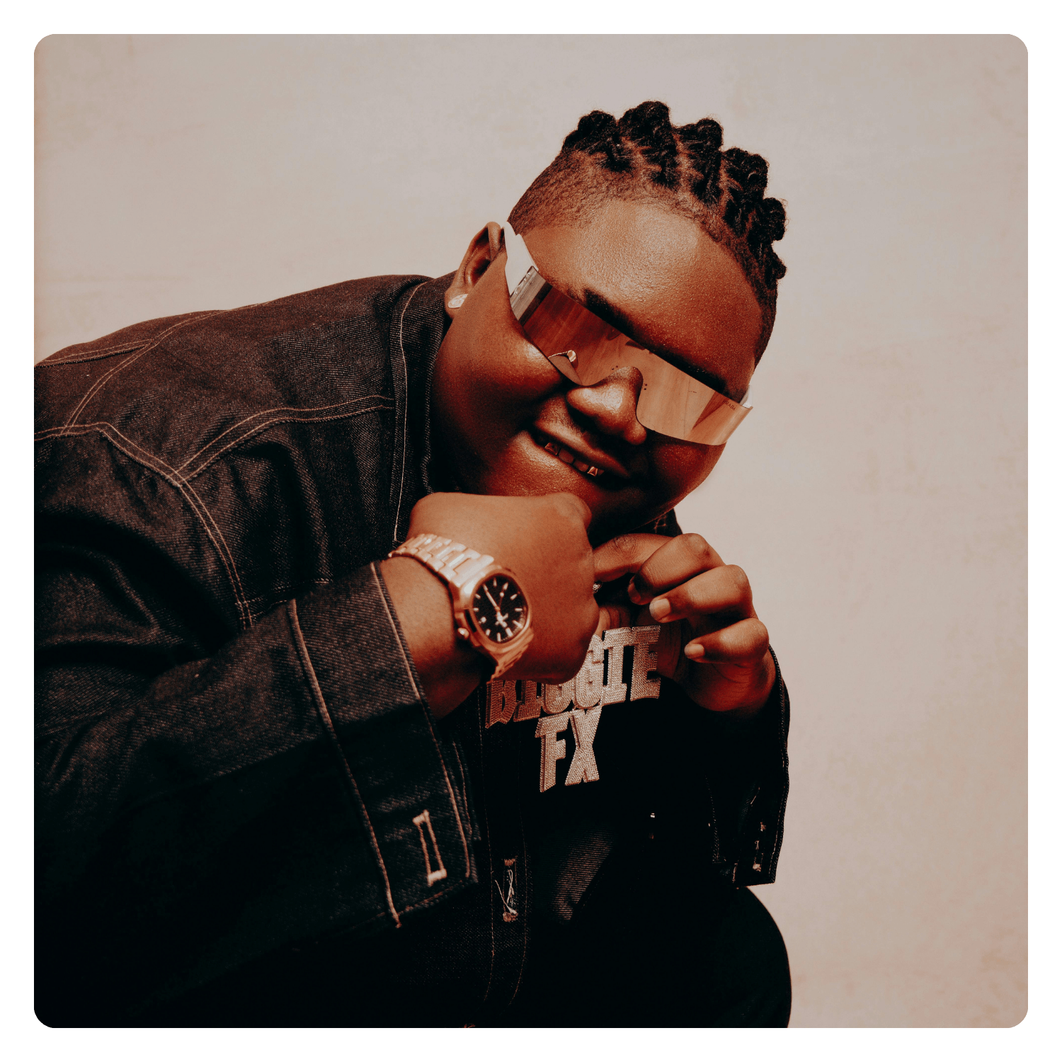 A young man wearing a black denim jacket, gold watch, and stylish sunglasses, smiling and looking at the camera.
