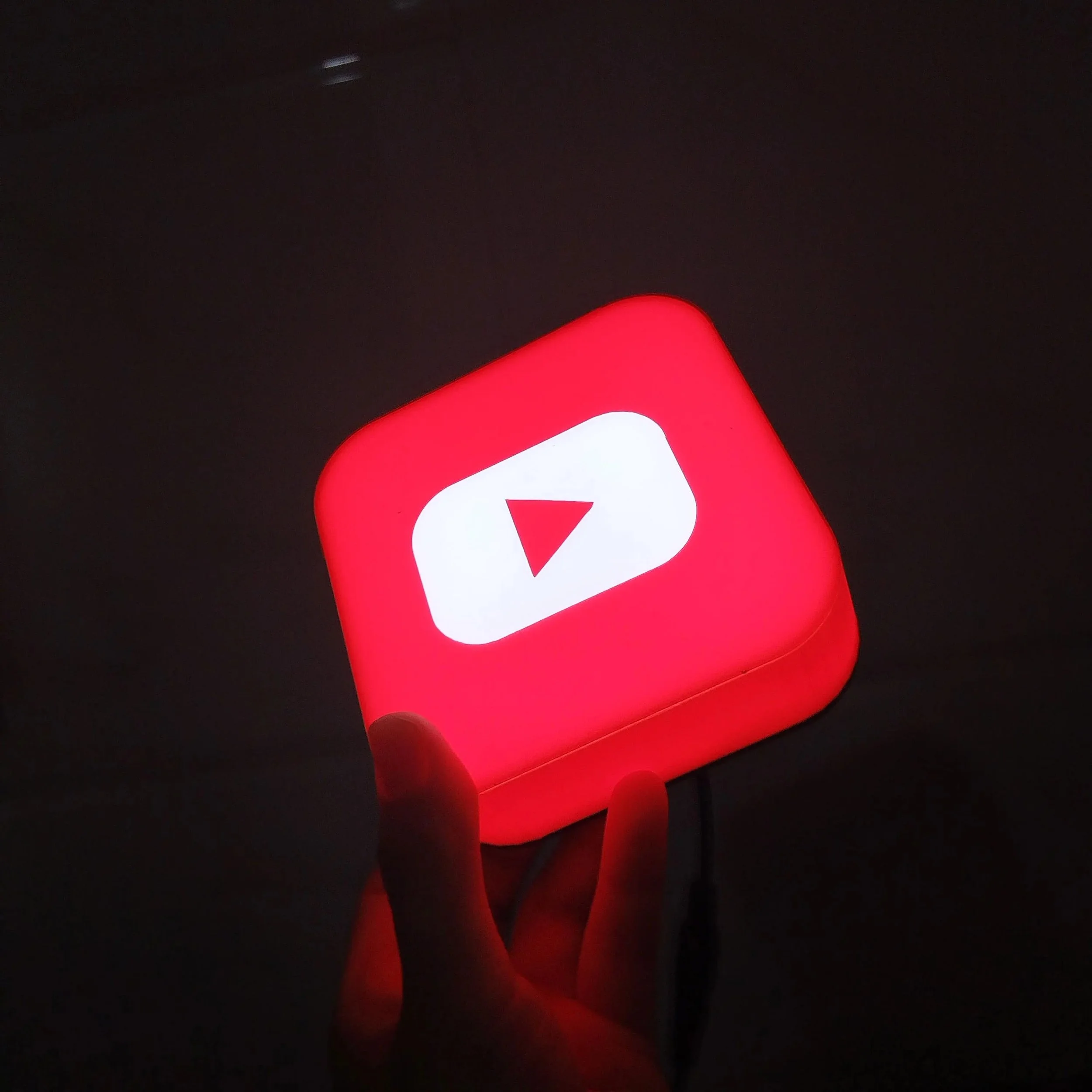 A person holding a red illuminated box with the YouTube play button logo.