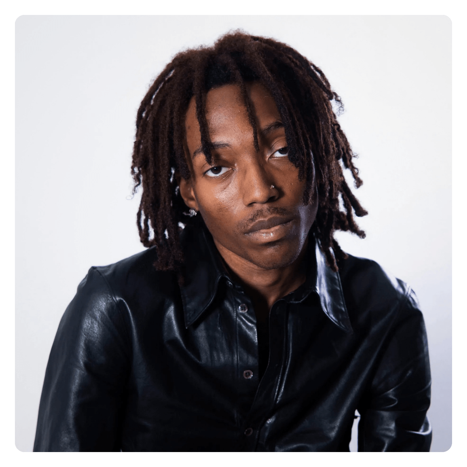 Portrait of a man with dreadlocked hair wearing a black leather shirt against a plain white background.