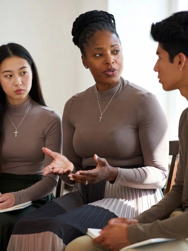 A female Kingdom Formation mentor is engaged in a serious discussion during a mentorship session, with mentees seated in chairs.