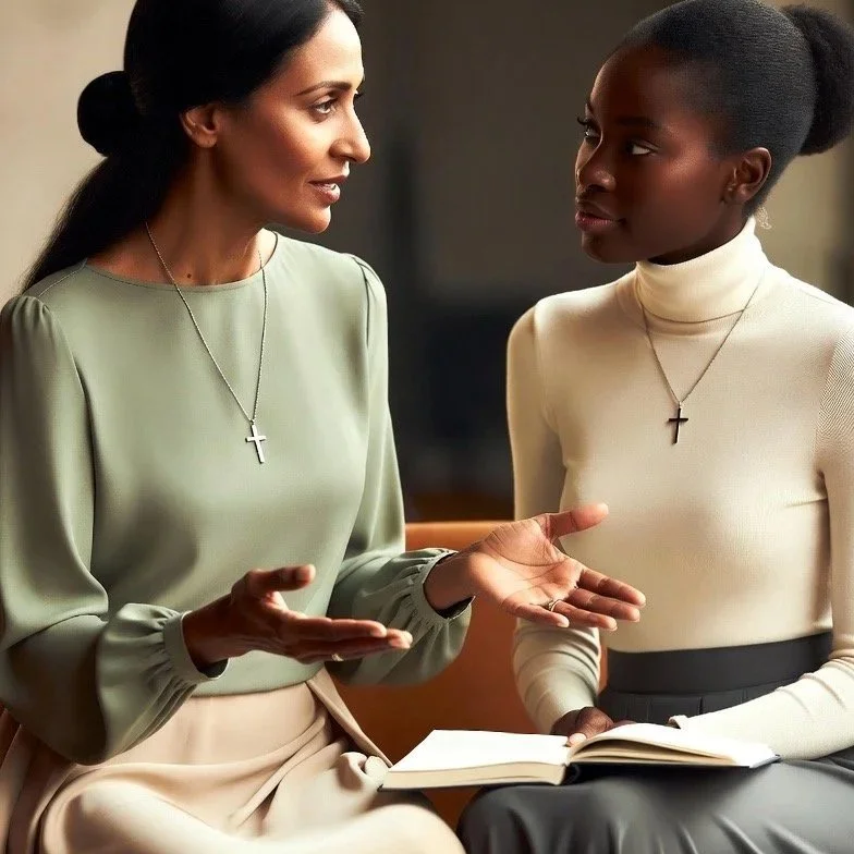 Two women, one older and one younger, engaged in a serious conversation in an indoor setting. Both are wearing necklaces with cross pendants, and the younger woman is holding a notebook.