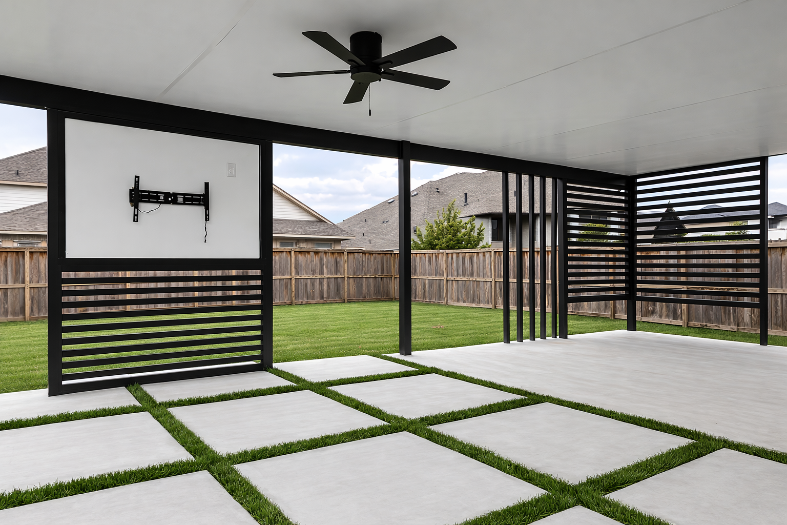 Empty backyard patio with concrete pavers and grass, black pergola with horizontal slats on the side, ceiling fan, and a mount for a TV.