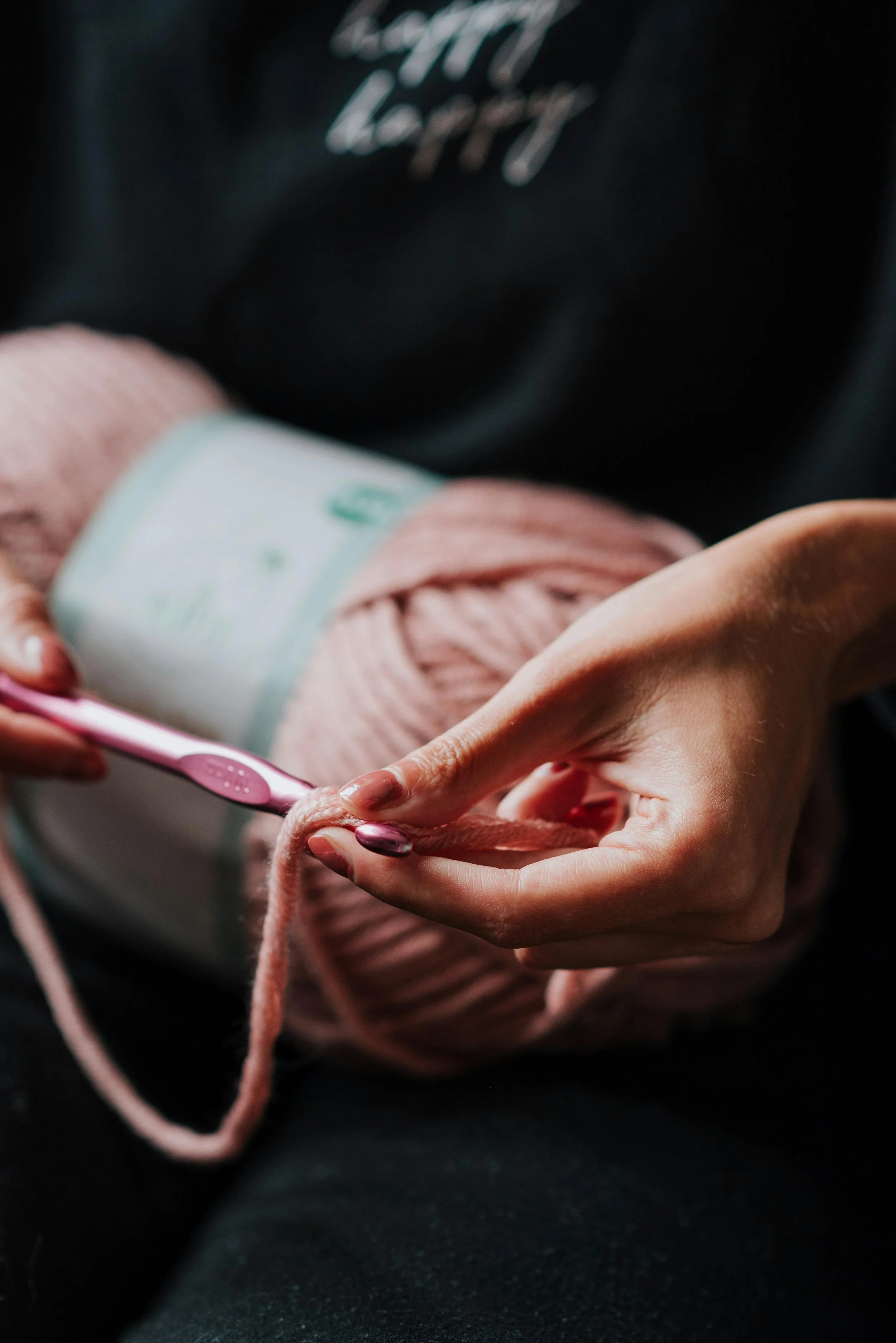 A person knitting with pink yarn, holding a knitting needle, with a ball of pink yarn in the background.