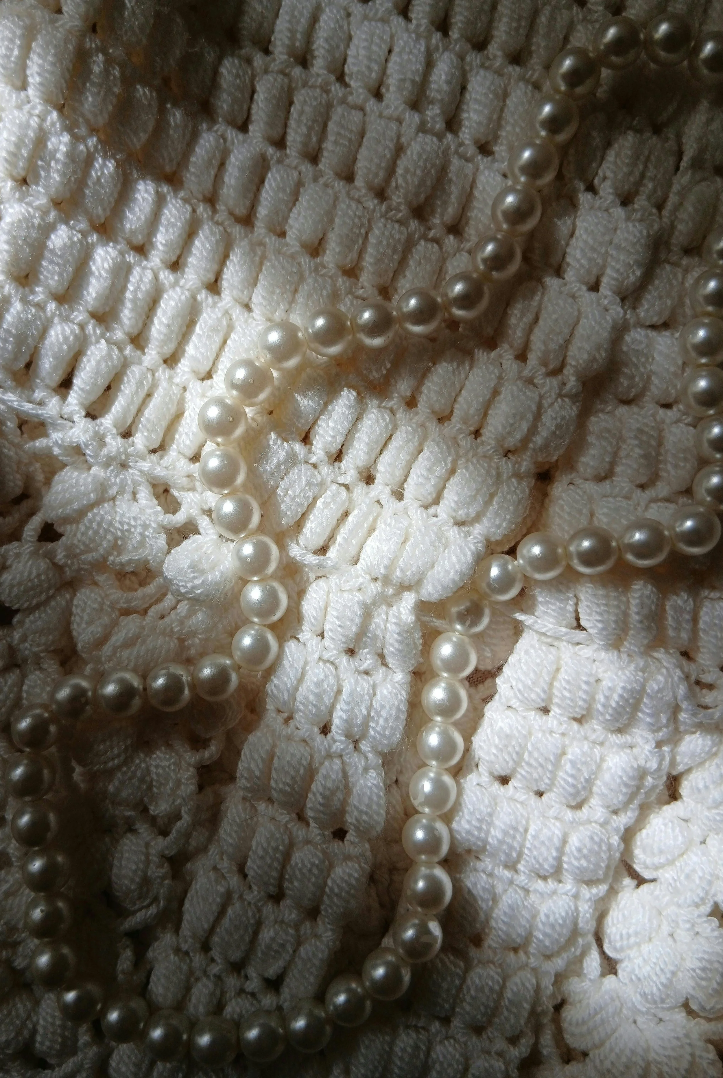 Close-up of a white textured fabric with a string of pearls draped over it.