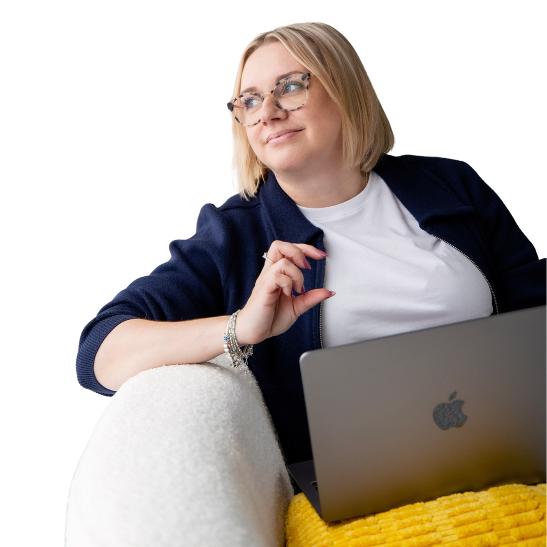 Sadie Finch with blonde hair and glasses looking thoughtfully to the side while sitting with a laptop on her lap.