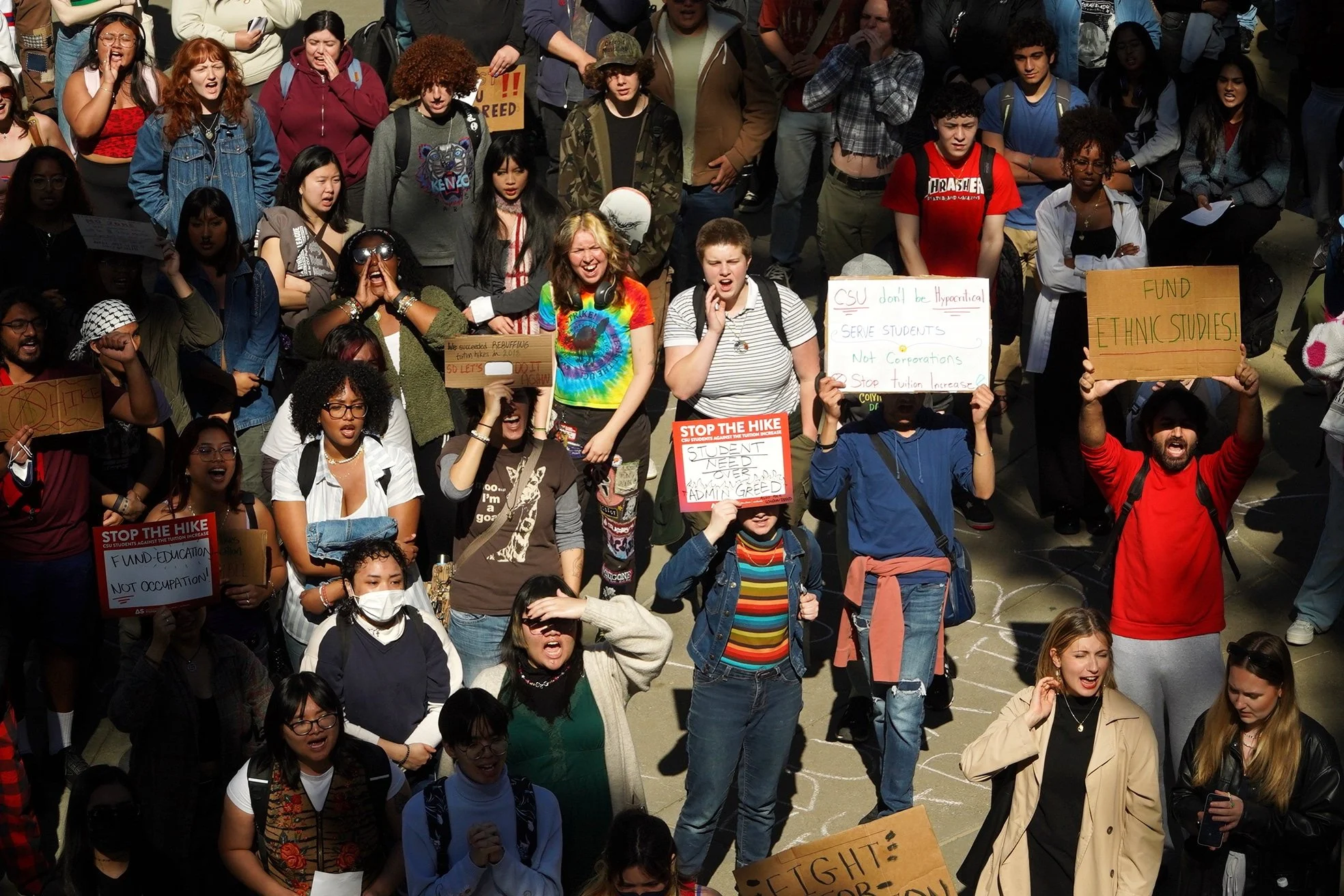 A large group of diverse students protesting, holding signs about education funding, tuition hikes, and ethnic studies at a rally.