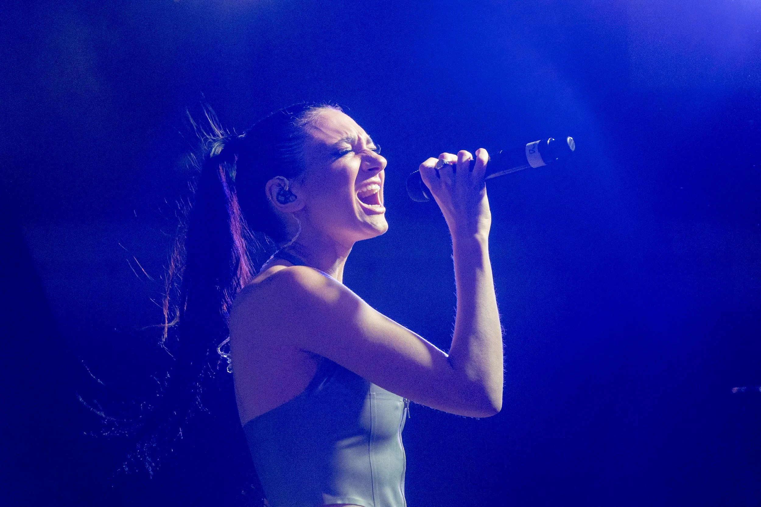 A woman singing passionately into a microphone on stage with blue lighting.