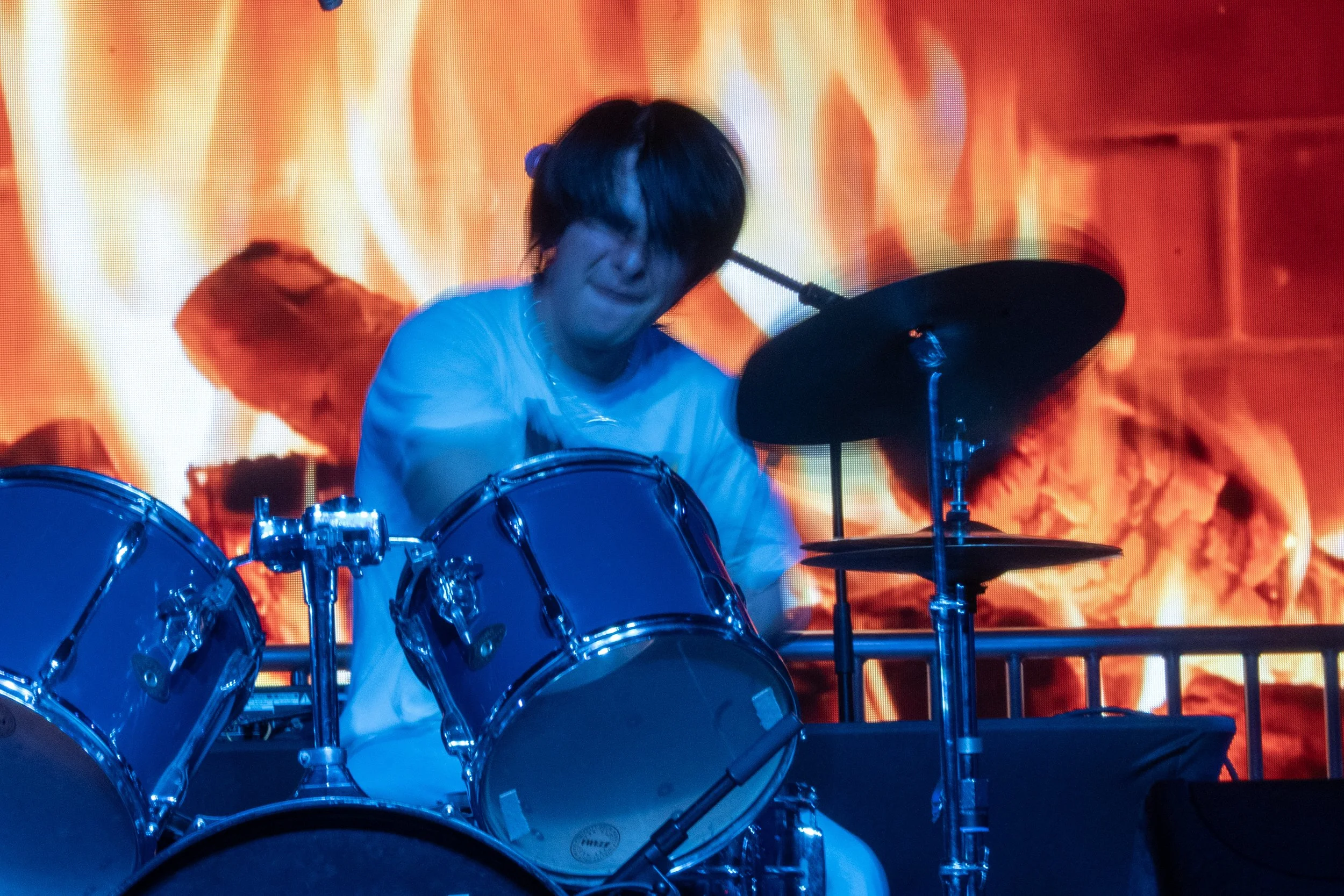Person playing drums on stage with a fiery background.